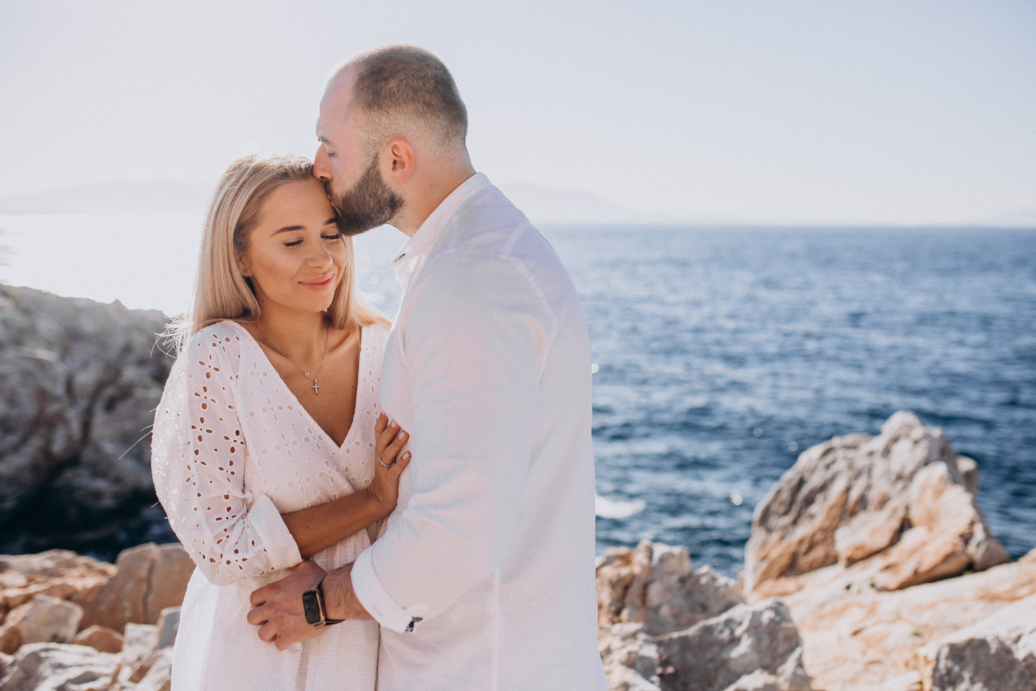 Couple enlacé au bord de la mer avec Love Explorers en France, moment tendre sur un littoral rocheux ensoleillé