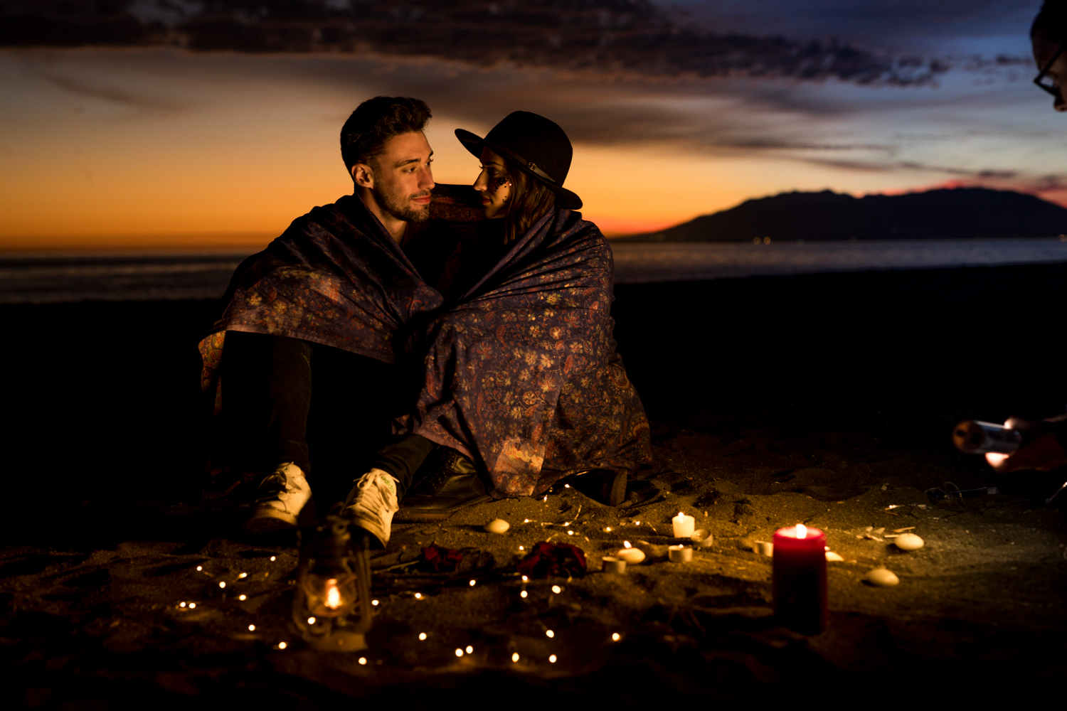 Couple enlacé sous couverture au coucher du soleil sur la plage en France, ambiance romantique Love Explorers